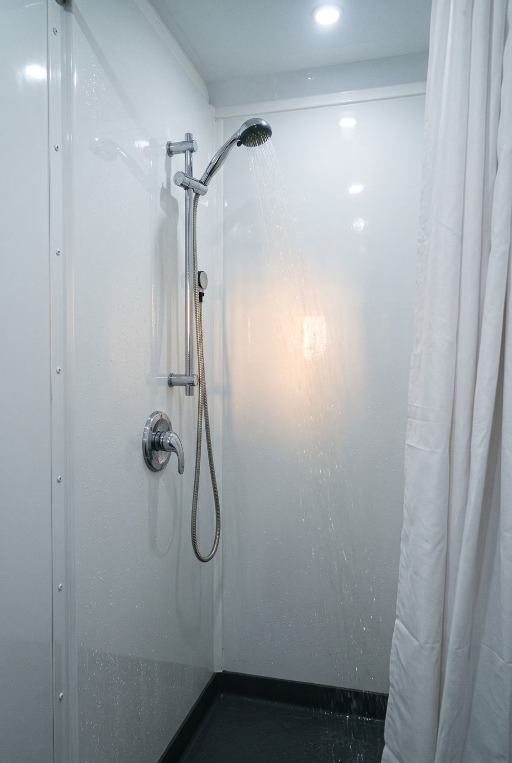 Chrome handheld showerhead on a slide bar with hot water running in a white molded stall