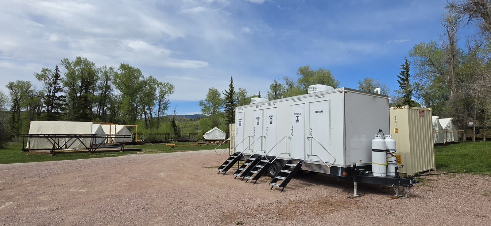 Four-room shower and laundry trailer beside a canvas wall-tent camp