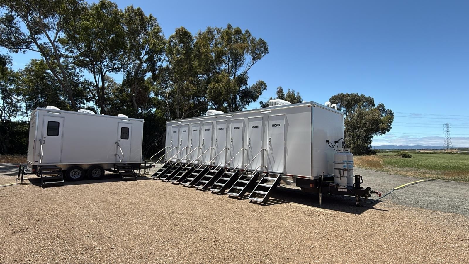 Eight-door shower trailer at a rural crew site with a second trailer and power lines behind