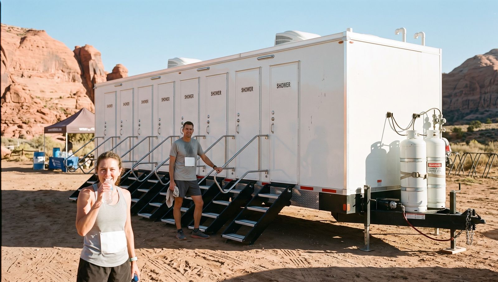 Trail runners at an eight-door shower trailer set at a Moab trailhead among red sandstone fins